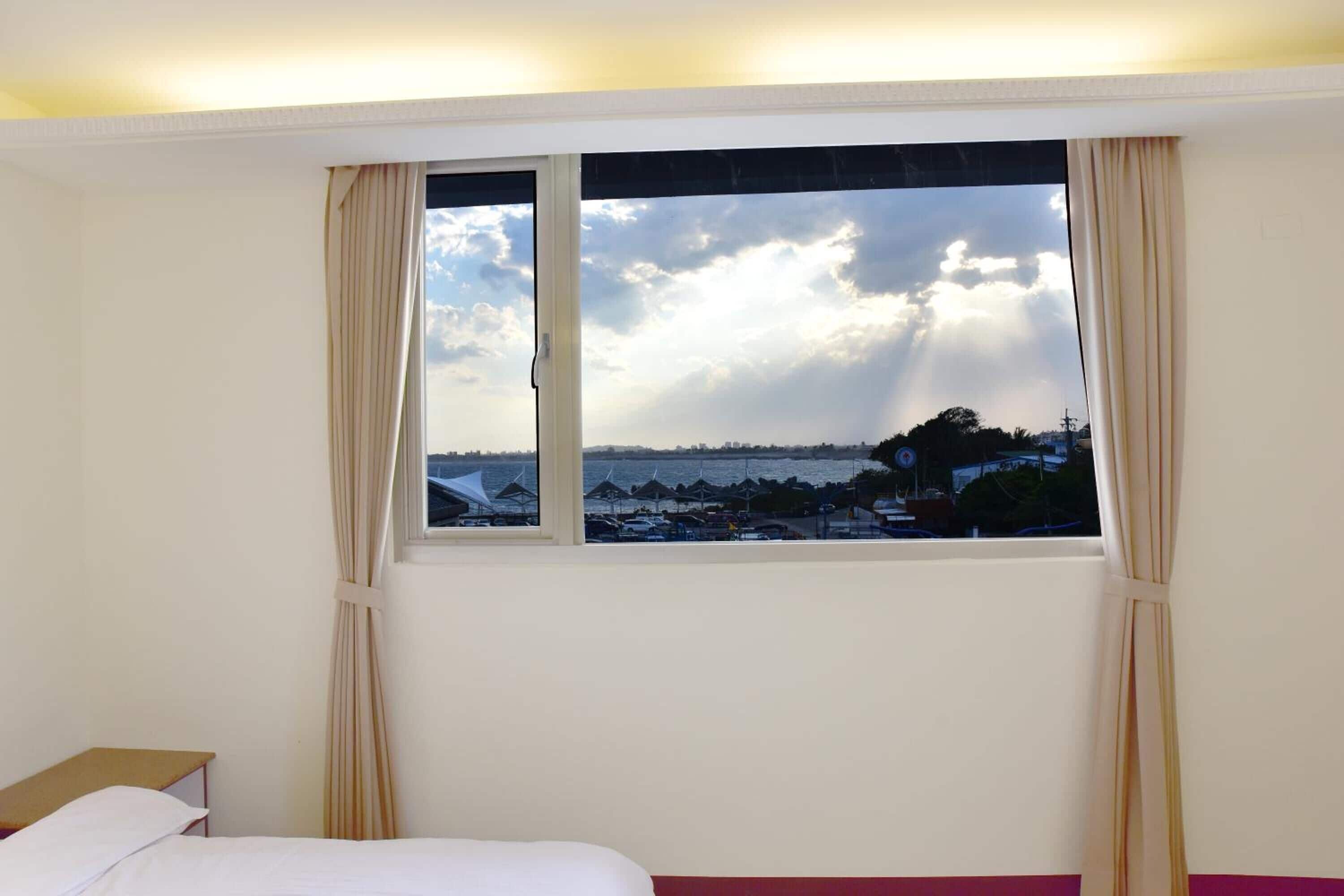 Une chambre d’hôtel avec un lit, une fenêtre avec des rideaux et une vue sur la plage et le paysage urbain.