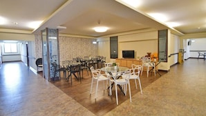 A spacious living area with a high ceiling, a dining table surrounded by chairs, a television, and a kitchen area. - Fugong Hostel (Taitung)