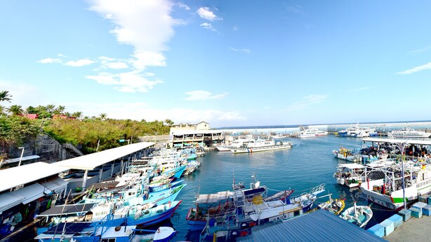 A marina with boats docked, a pier with people, and a building in the background. - Fugong Hostel (Taitung)