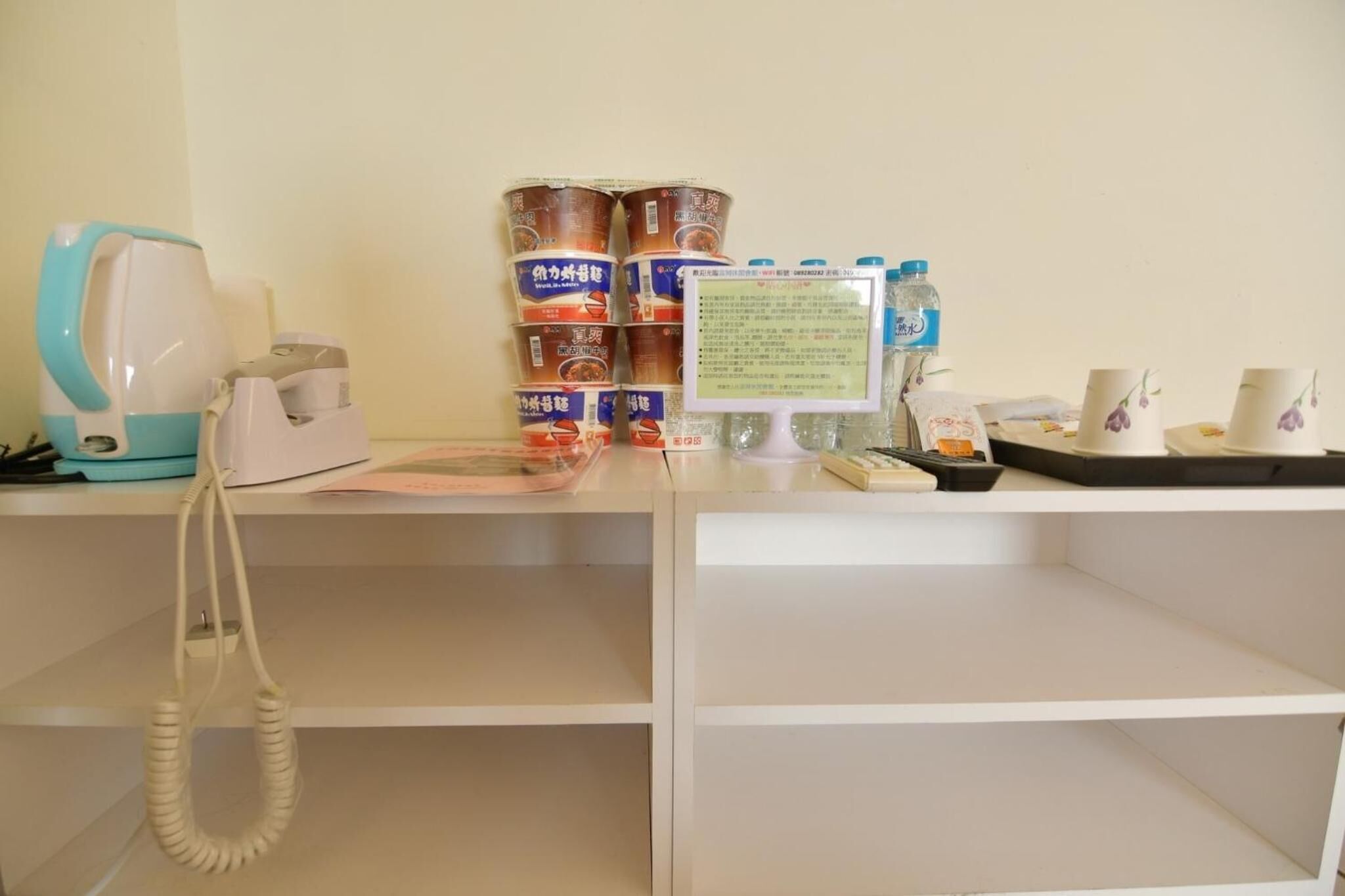 A reception desk with a telephone, a kettle, stacked cans, a water dispenser, and a sign.