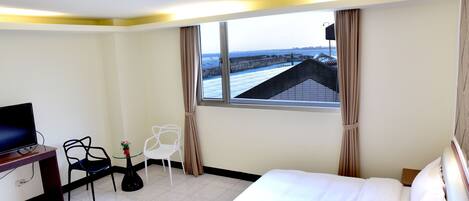 Habitación de hotel con cama, escritorio con televisor, silla, pequeña mesa con planta y ventana con vista a un puente.