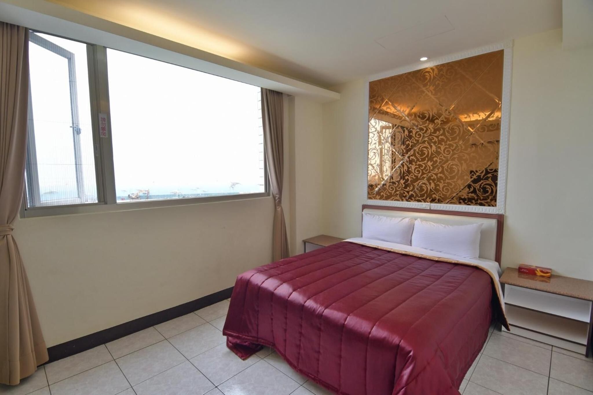 Una habitació d'hotel amb un llit gran, una tauleta de nit i una finestra amb cortines.