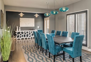 A dining area with a dark wooden table, teal upholstered chairs, and pendant lights.