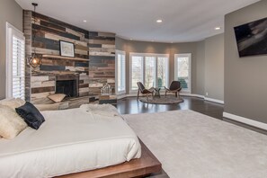 A modern bedroom with a large bed, a fireplace, and a seating area with chairs.