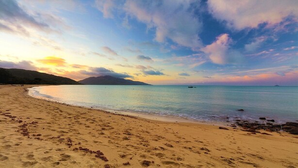 A beach with footprints leading to the water, a boat in the distance, and a mountain in the background. - 'IslandView' The Perfect Holiday Home (Hideaway Bay)