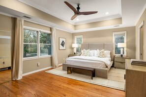 A bedroom with a large bed, a ceiling fan, and two windows.