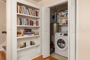 A laundry room with a washing machine, shelves with books, and a water heater.