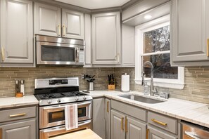 A kitchen with stainless steel appliances, a tiled backsplash, and a window with a view.