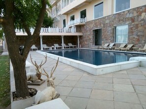A swimming pool with lounge chairs and a stone wall. - Fateh Niwas (Udaipur)