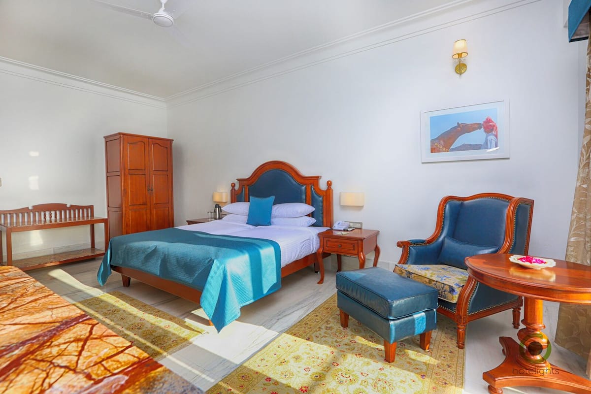A hotel room with a bed, a wooden wardrobe, a desk, a chair, and a small table.