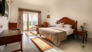 A hotel room with a bed, a desk, a chair, a TV, and a view of the outdoors. - Fateh Niwas (Udaipur)
