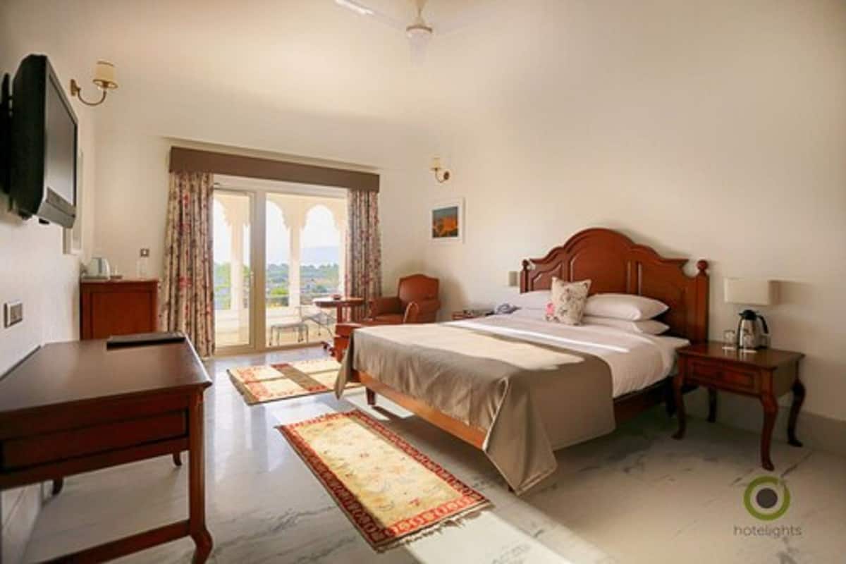 A hotel room with a bed, a desk, a chair, a TV, and a view of the outdoors.