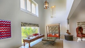 A spacious living room with a high ceiling, large windows, a wooden bench, a sofa, and a decorative chair. - Fateh Niwas (Udaipur)