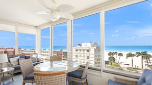 Un balcon agrémenté de meubles en osier, d’une table en verre et offrant une vue sur la plage et l’océan.