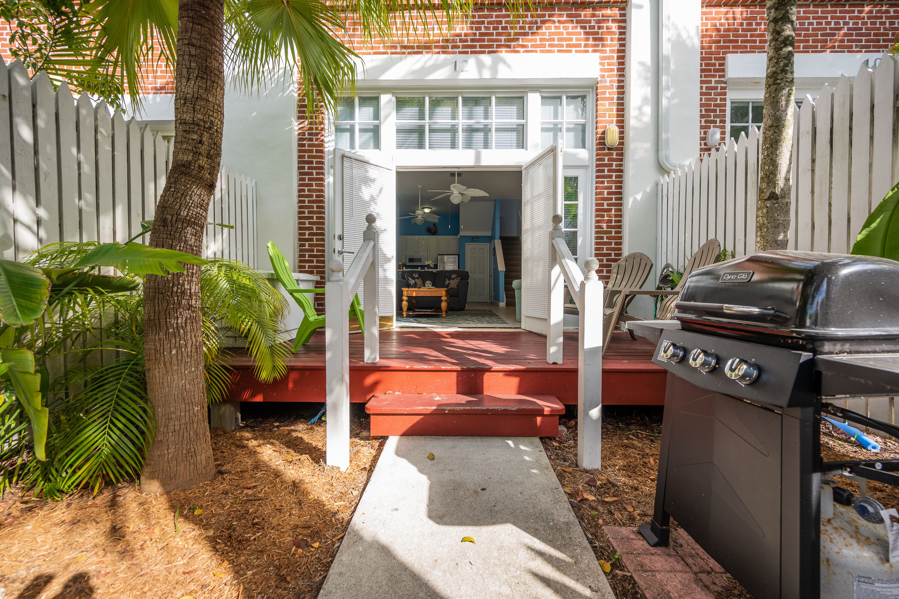 A backyard with a barbecue grill, a white fence, and a house number 12.