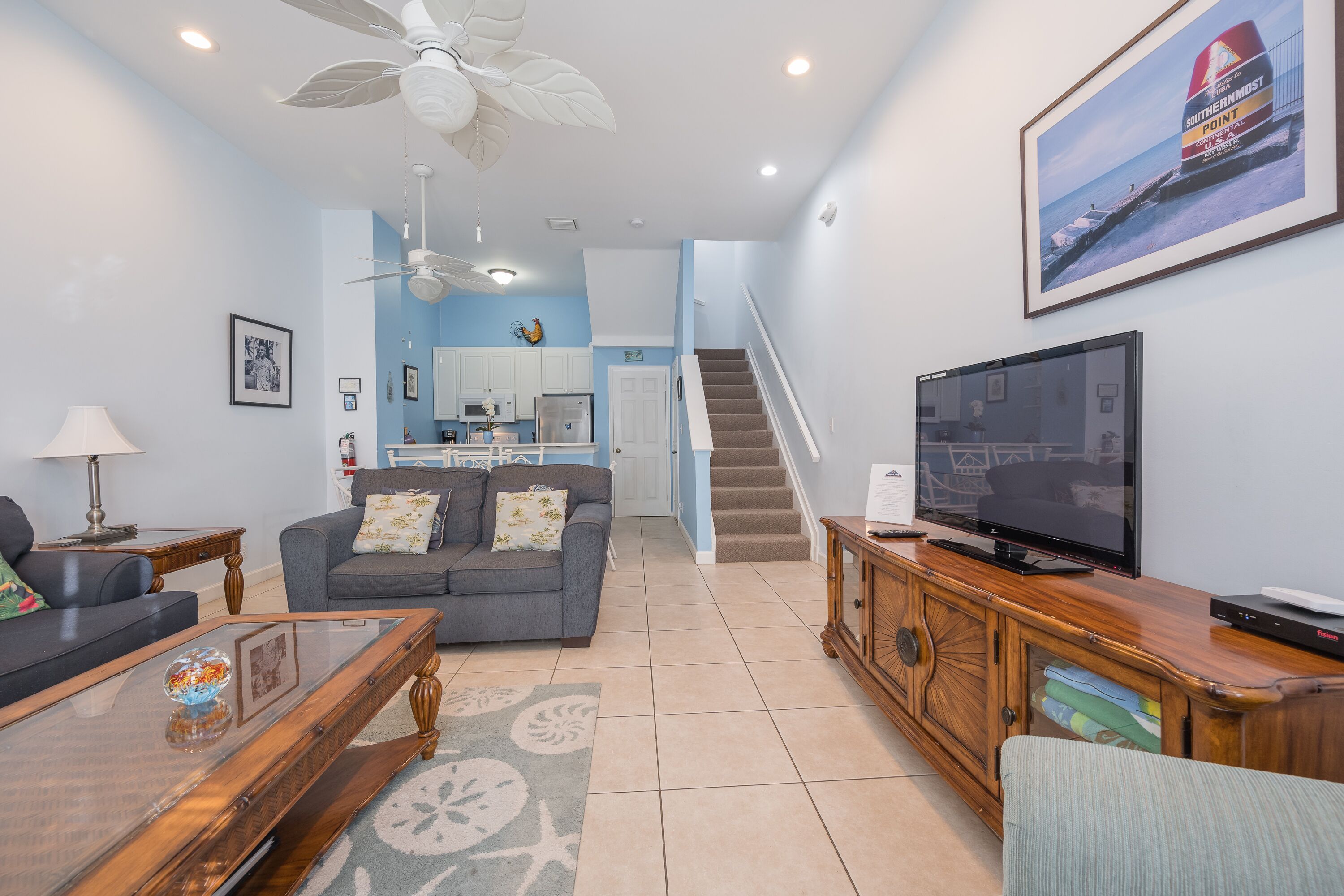 A living room with a sofa, coffee table, TV, and a staircase leading to a kitchen.