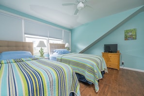 Quarto com duas camas, ventilador de teto, televisão sobre uma cômoda e janela com persianas.