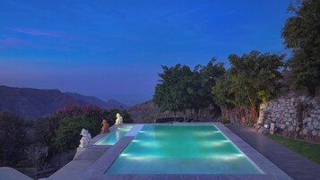 Una piscina infinita rectangular con un muro de piedra a un lado y vistas de montañas al fondo.