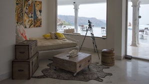 Une pièce comprenant un lit, une table basse, un trépied et donnant sur l’extérieur.
