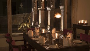 Une table à manger dressée avec des bougies, des serviettes et des couverts, avec en arrière-plan des colonnes de pierre et une statue.