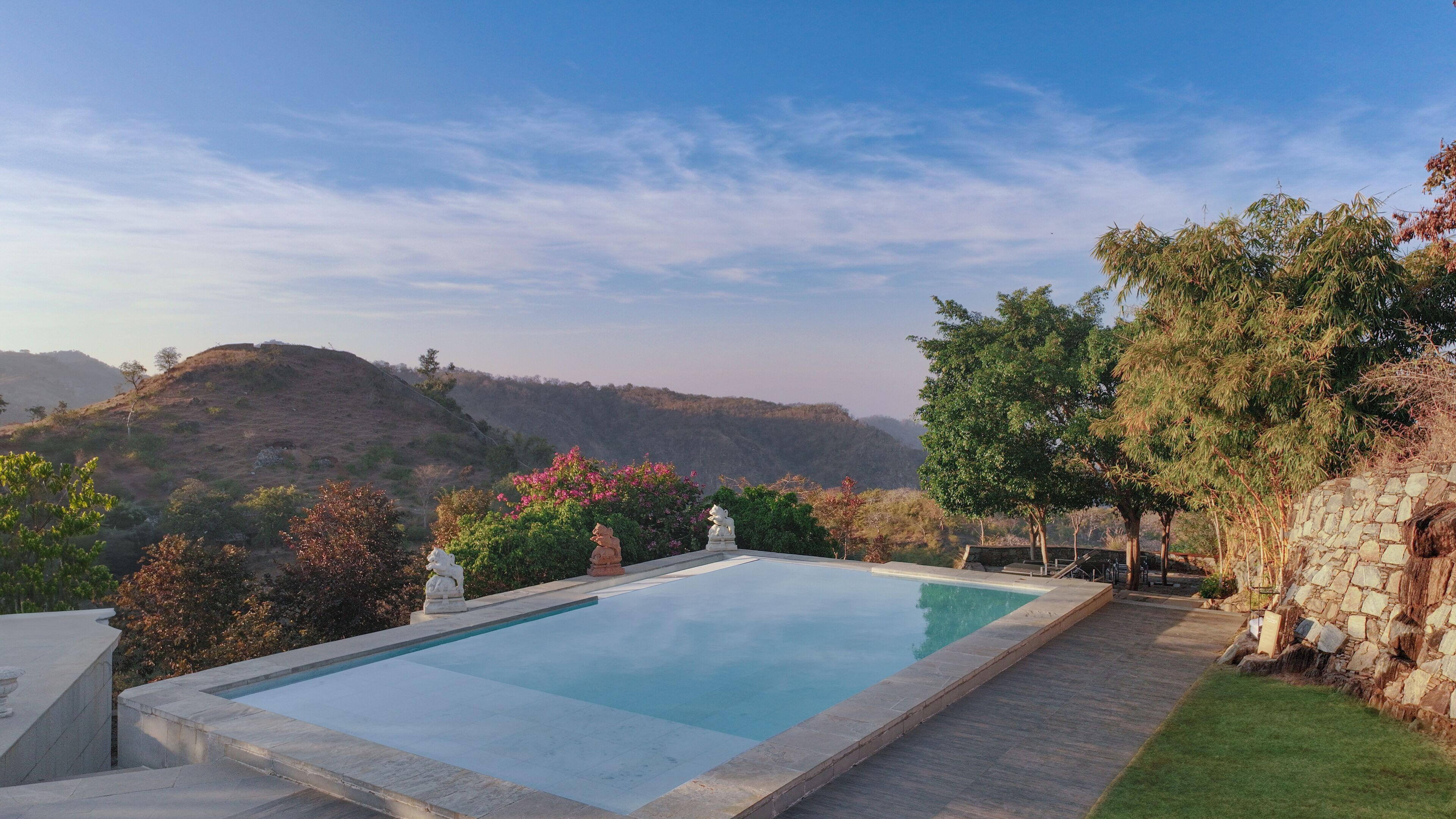 A rectangular swimming pool with a stone border, surrounded by a stone wall and a grassy area.