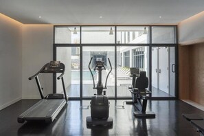 Un gimnasio con caminadora, elíptica y bicicleta estática, ventanas amplias y vistas al exterior.