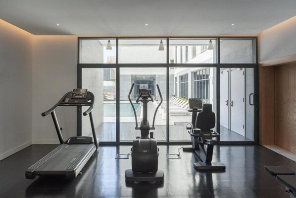 A gym with a treadmill, elliptical, and stationary bike, large windows, and a view of the outside. - DELTA HOTEL APARTMENTS (Sabah Al Salem)