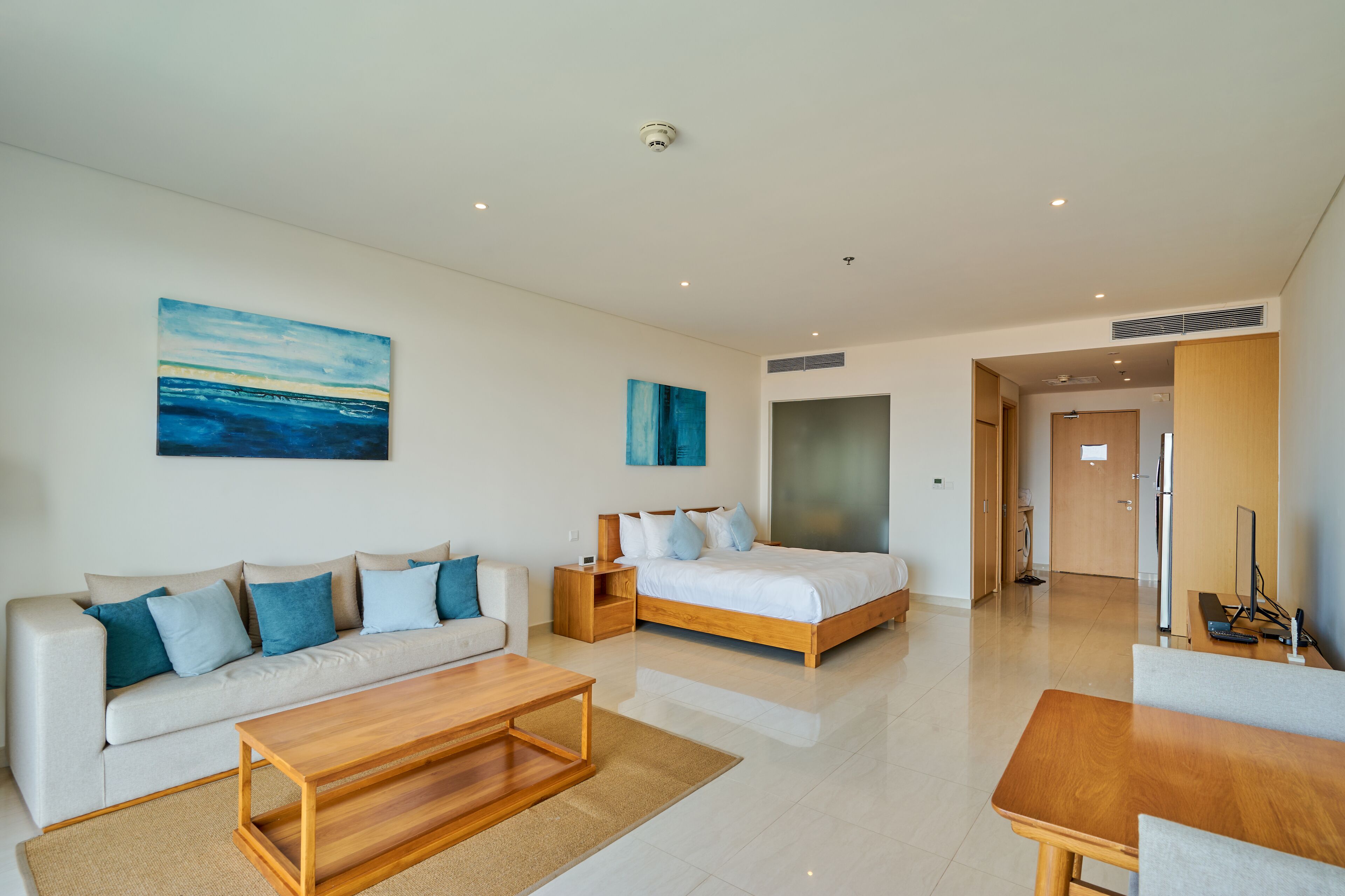 Quarto de hotel moderno com sofá, cama, mesa de centro de madeira e televisão.
