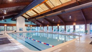 An indoor swimming pool with a wooden ceiling, clear windows, and lounge chairs.