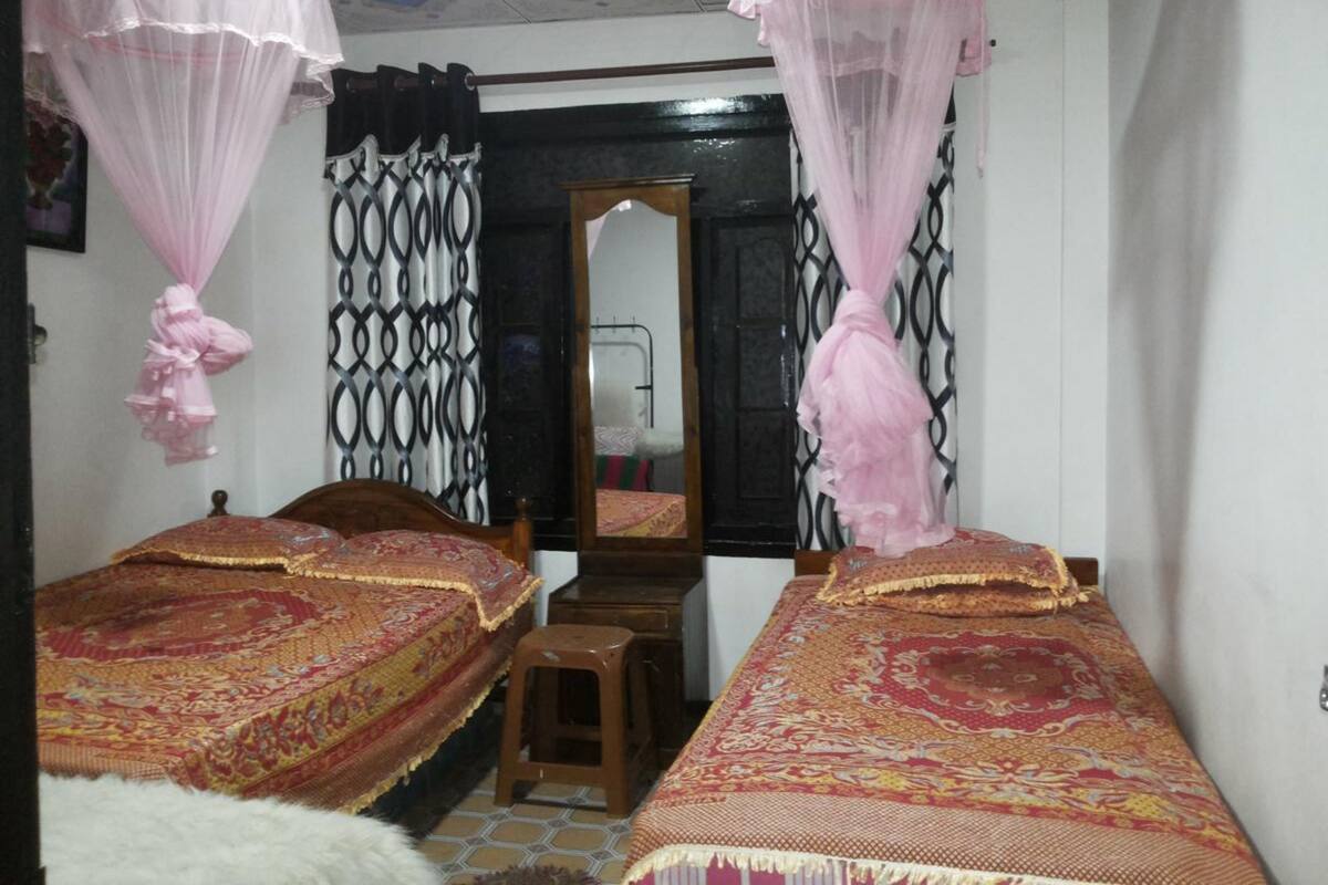 A room with two beds, a mirror, and a window with patterned curtains.