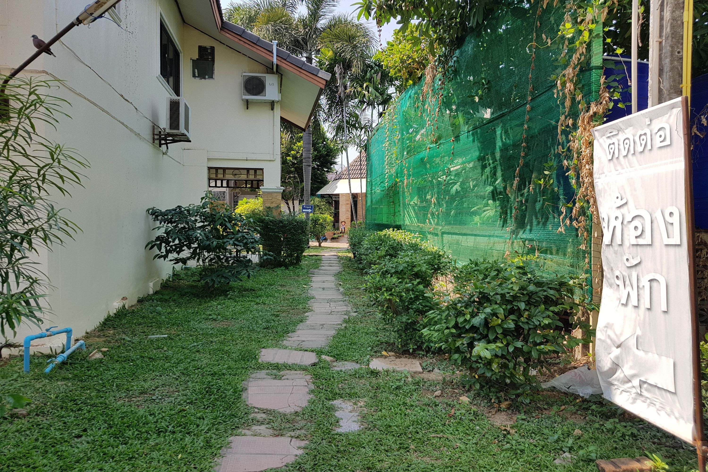 A narrow pathway leading to a building with a green netting on one side.