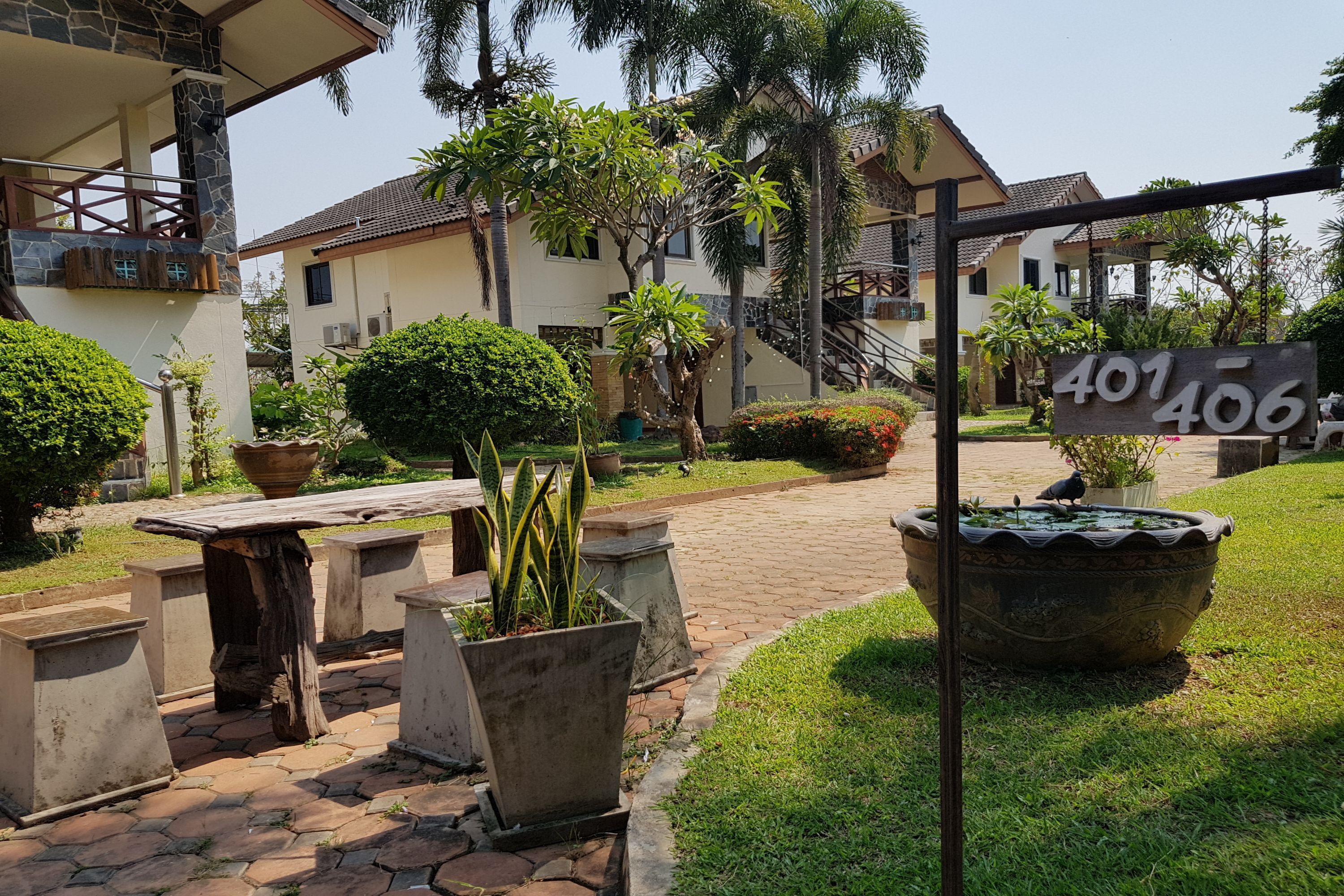 Zona residencial con un letrero que dice "401 406", un camino pavimentado, plantas en macetas y un pájaro en una valla.