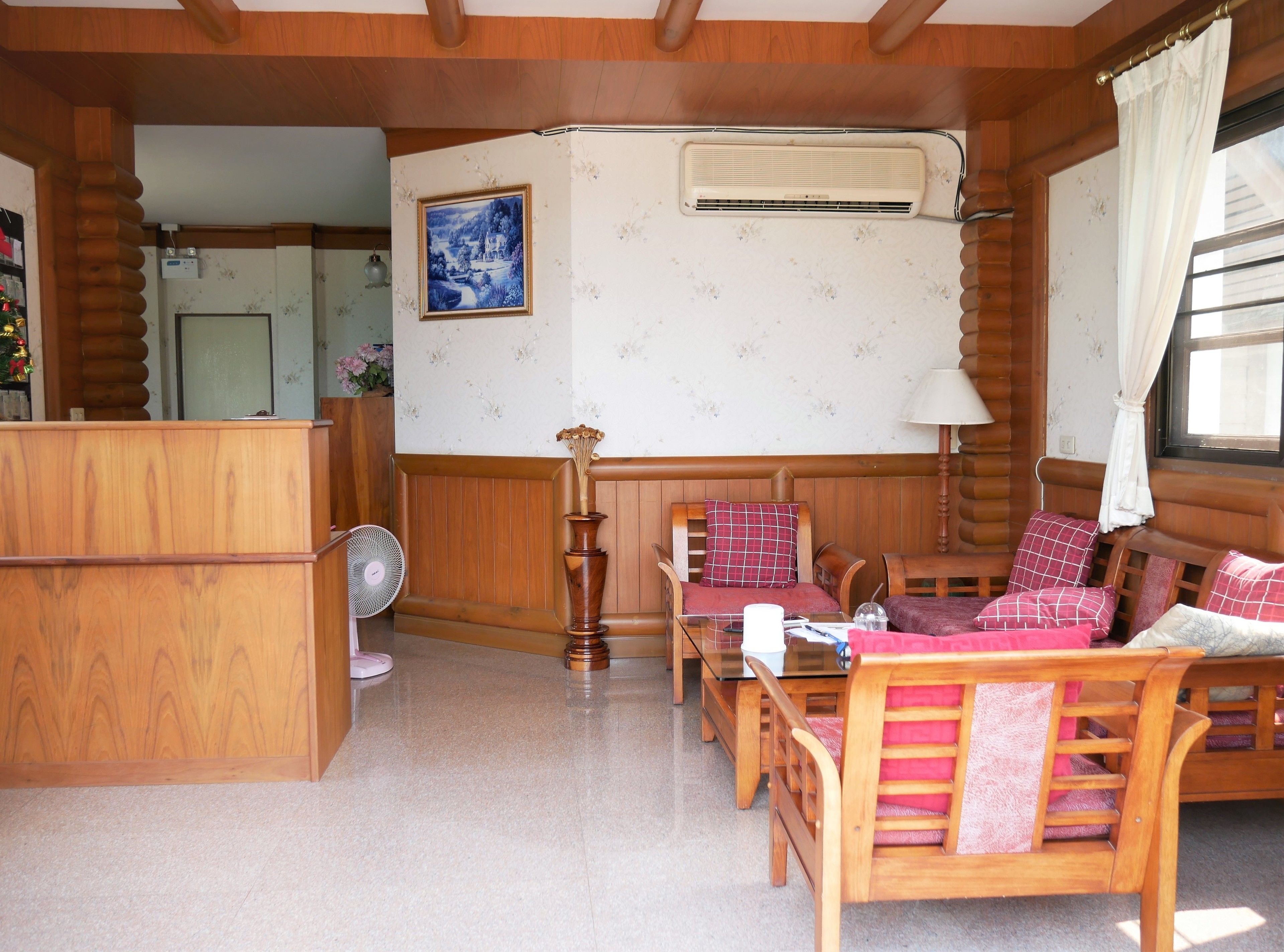 A cozy cabin interior with wooden walls and furniture, a fan, a painting, and a window with curtains.