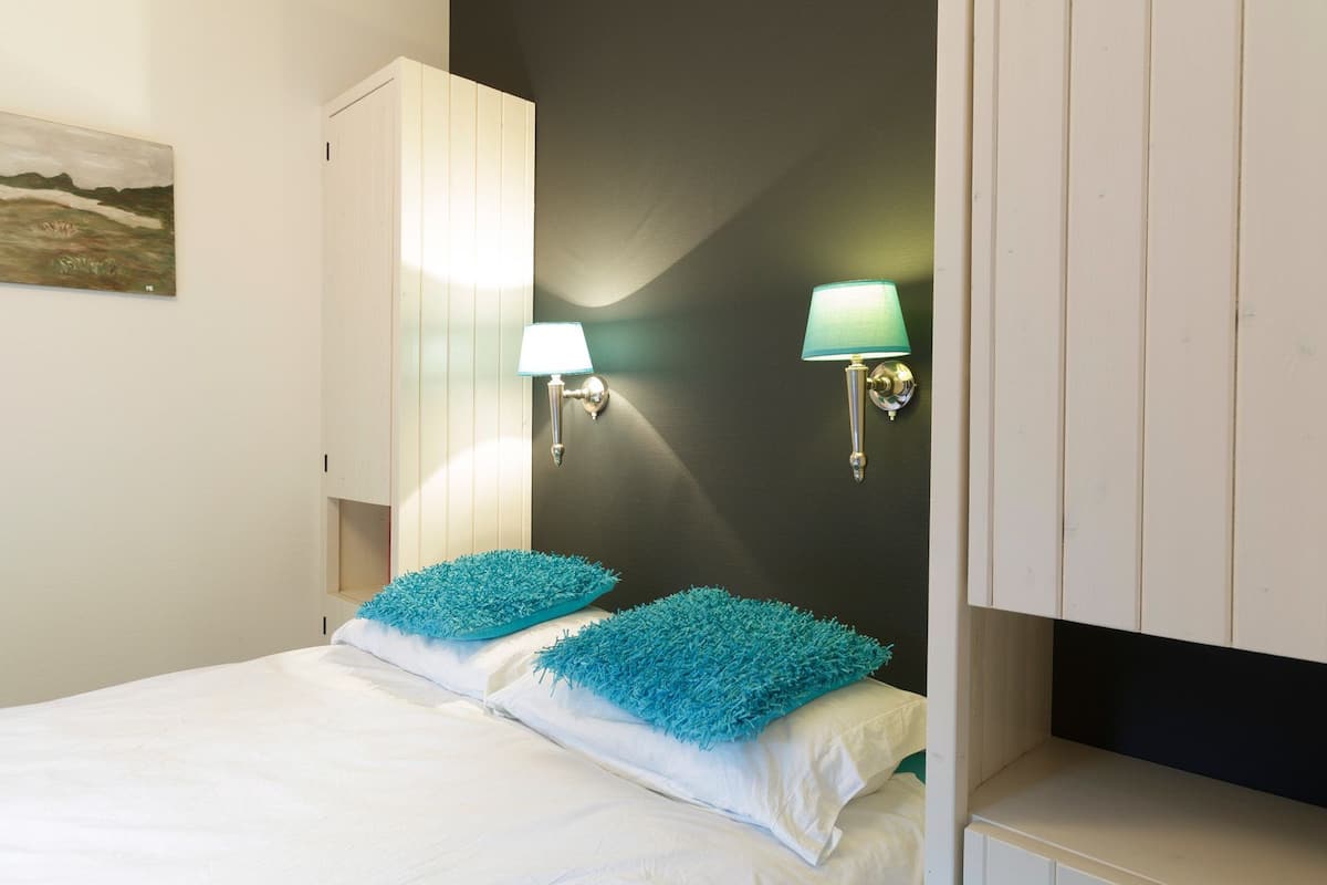 A bedroom with a bed, two wall-mounted lamps, and a painting on the wall.