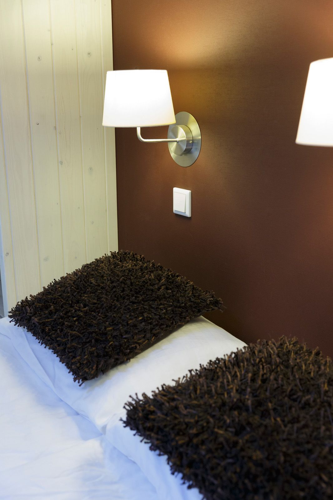 Ein Zimmer mit zwei dunkelbraunen, gepolsterten Kopfteilen, einem weißen Lichtschalter und Wandleuchten.