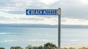 Señal que indica acceso a la playa, con vista al mar y montañas a lo lejos.