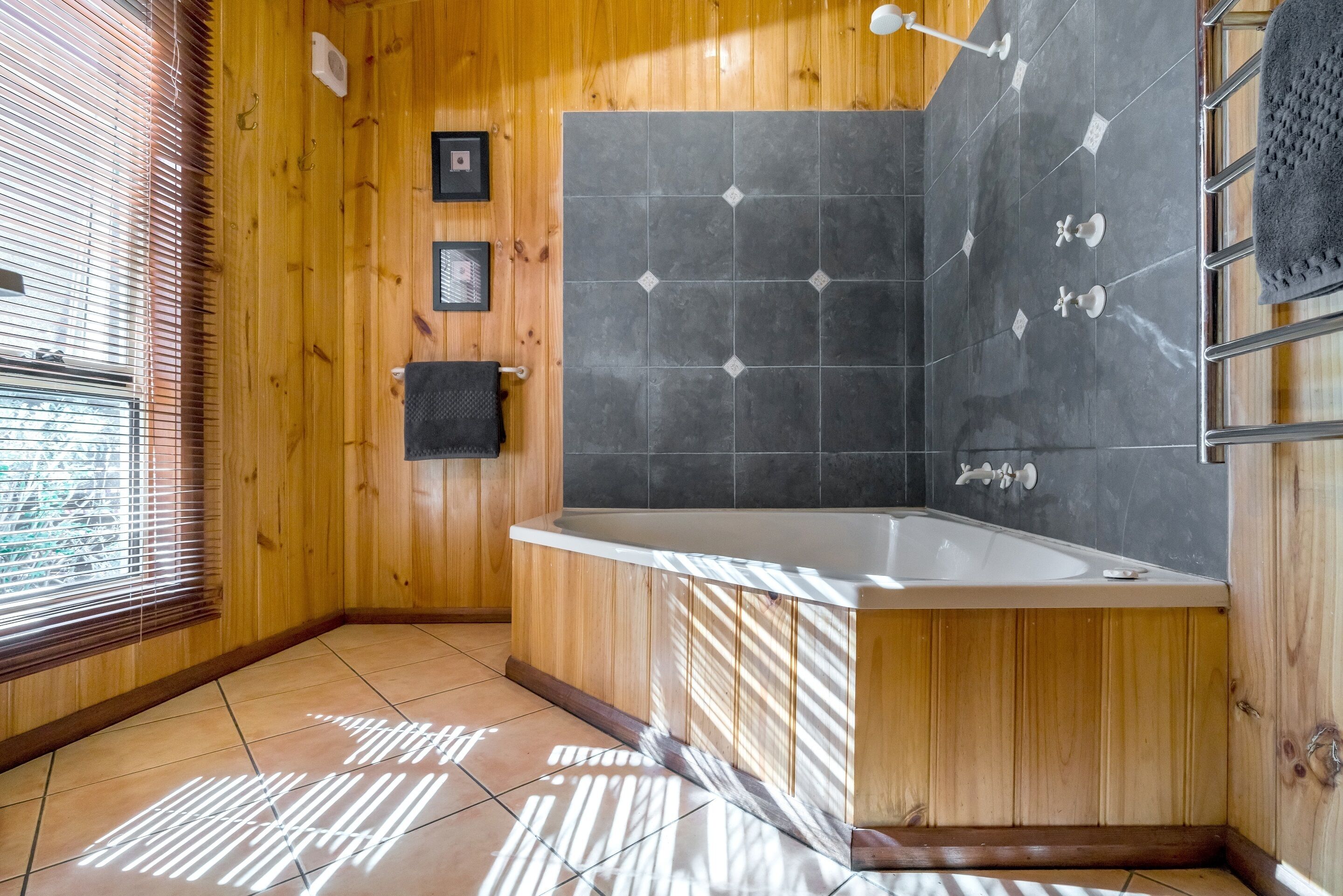 Un bagno con rivestimenti in legno, una vasca freestanding, piastrelle e una finestra con persiane.