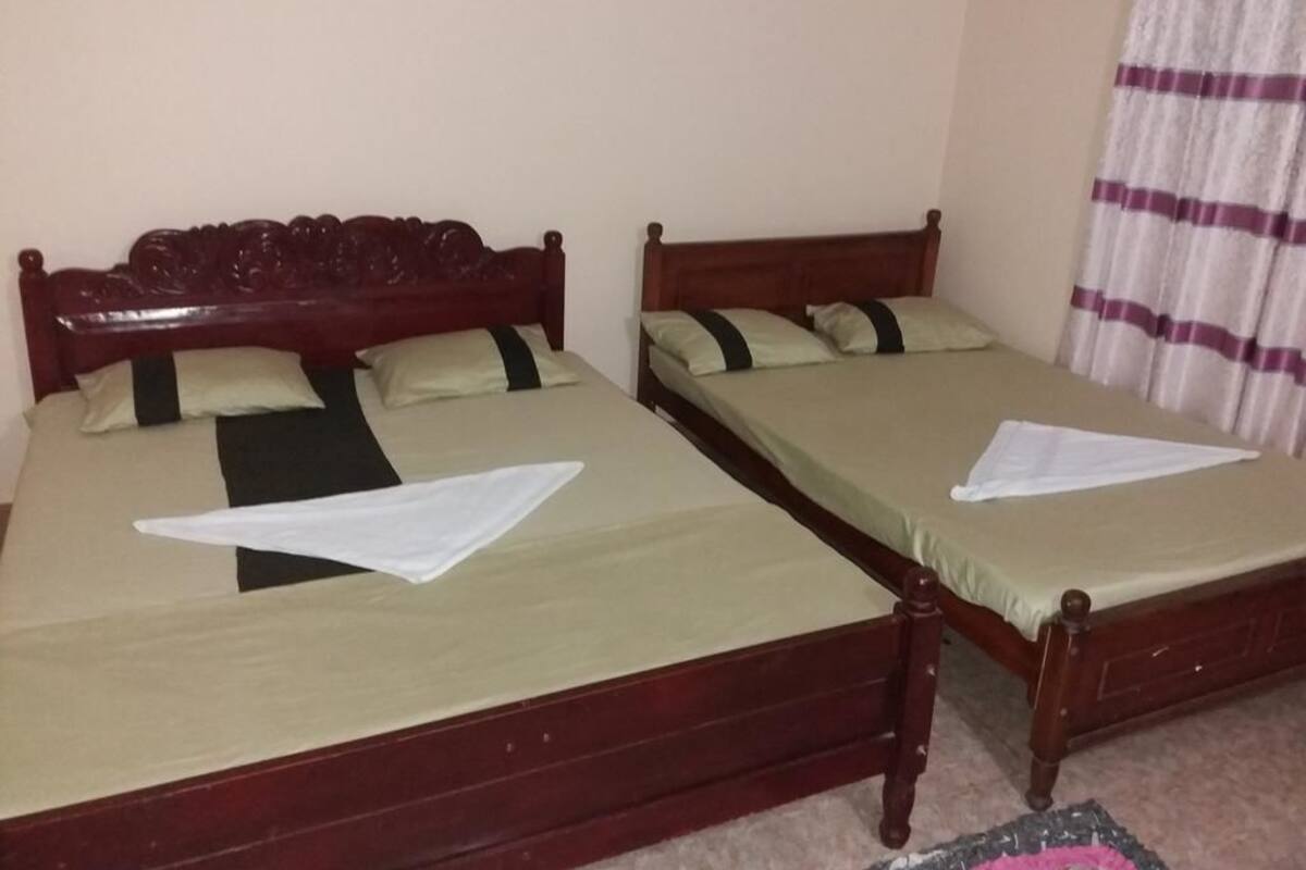 Two wooden beds with green bedsheets and pillows, a white towel, and a striped curtain.