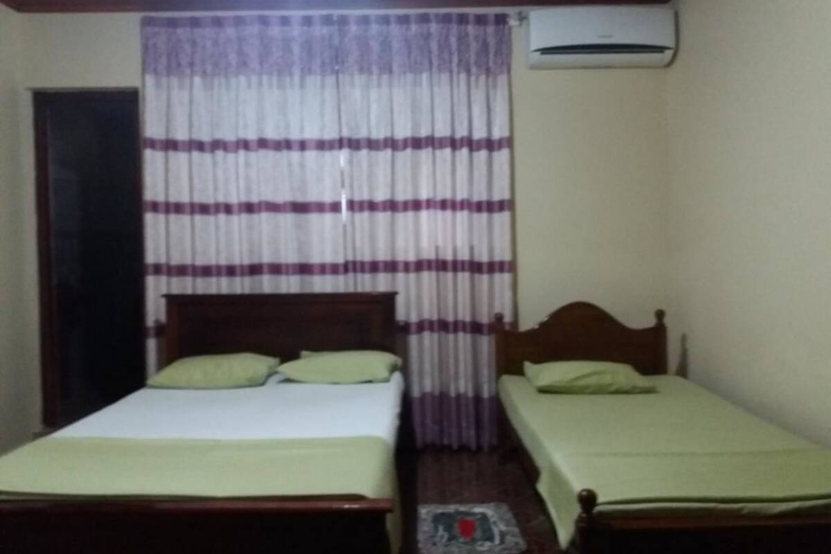 A small room with two single beds, a wooden headboard, a curtain with horizontal stripes, and an air conditioning unit on the wall.