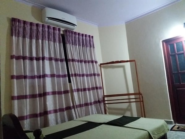 A room with a bed, an air conditioner, a window with purple curtains, and a door. - Italiano Restaurans (Thotagamuwa)