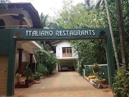 An entrance to Italian restaurants with a sign, a covered walkway, and surrounding greenery.