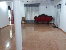 A hallway with a polished floor, a red upholstered sofa, a white pillar, and a door in the background.
