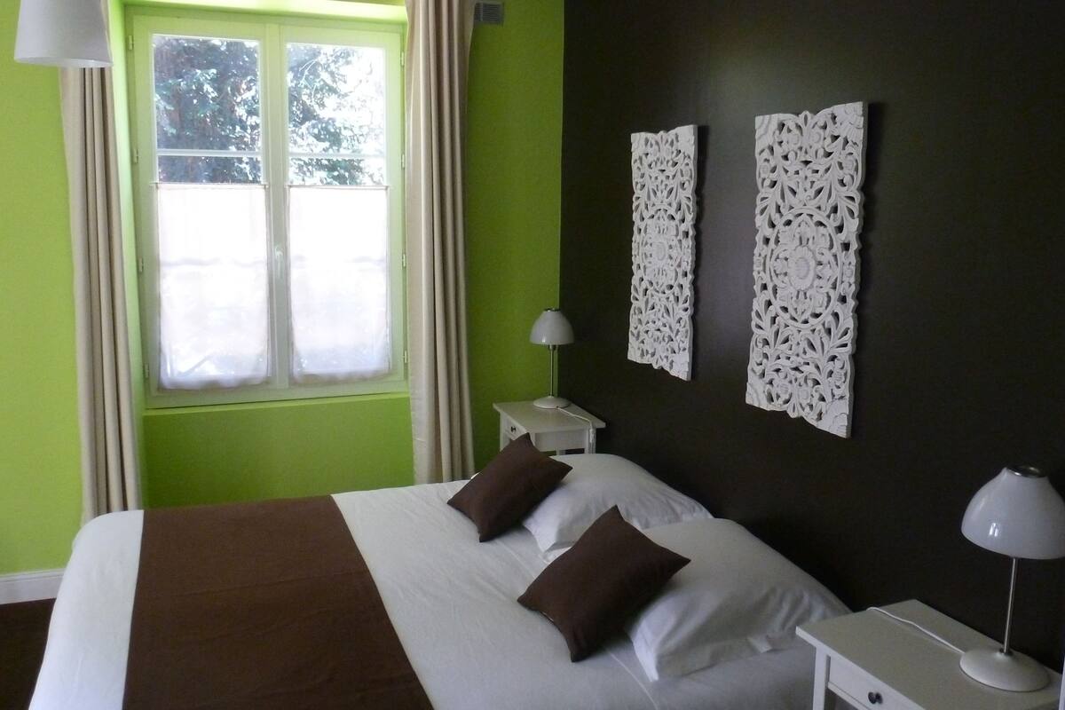 A hotel room with a bed, two bedside tables with lamps, a window with curtains, and decorative wall panels.