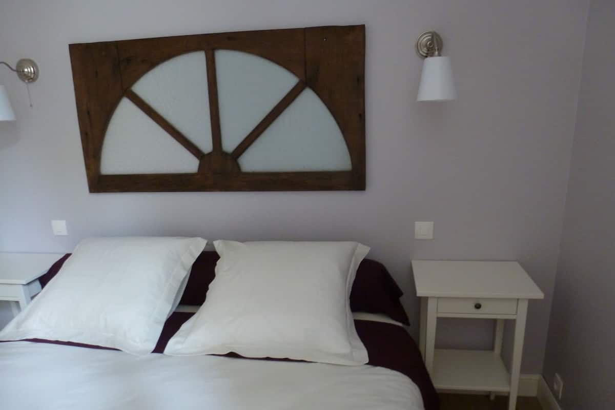 A bedroom with a bed, two nightstands, a wall-mounted light fixture, and a decorative wooden panel above the bed.