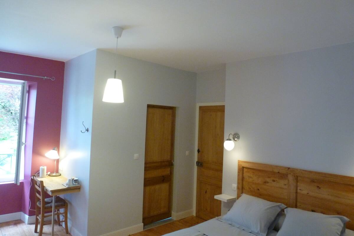 A bedroom with a wooden headboard, a desk with a chair, and a window.