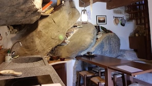 A rustic kitchen with stone walls, a wooden table, and a hanging light fixture. - Alla Battuta (Sansepolcro)