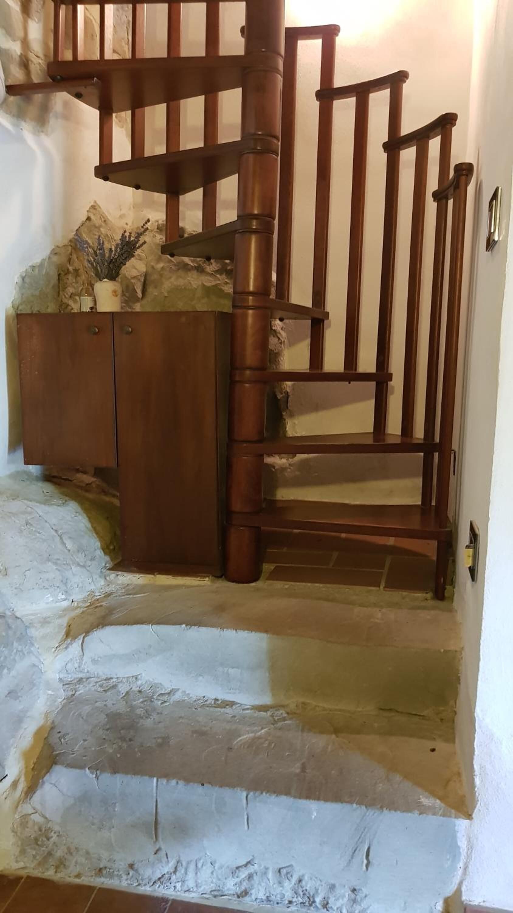 A wooden staircase with a handrail, leading to a landing area with a cabinet and decorative items.