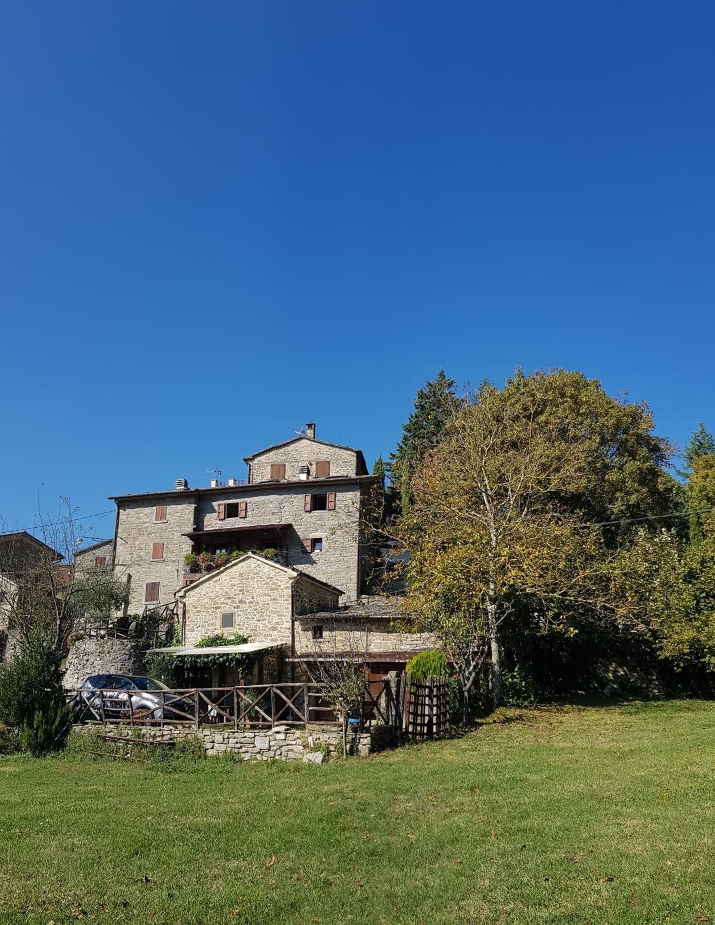 A stone building with multiple levels and a sloped roof, surrounded by a grassy area and trees.