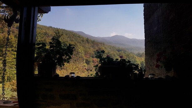 A room with a stone wall and a view of a forested mountain range. - Alla Battuta (Sansepolcro)
