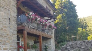 A stone building with a balcony adorned with flowers, a wooden fence, and a stone roof. - Alla Battuta (Sansepolcro)